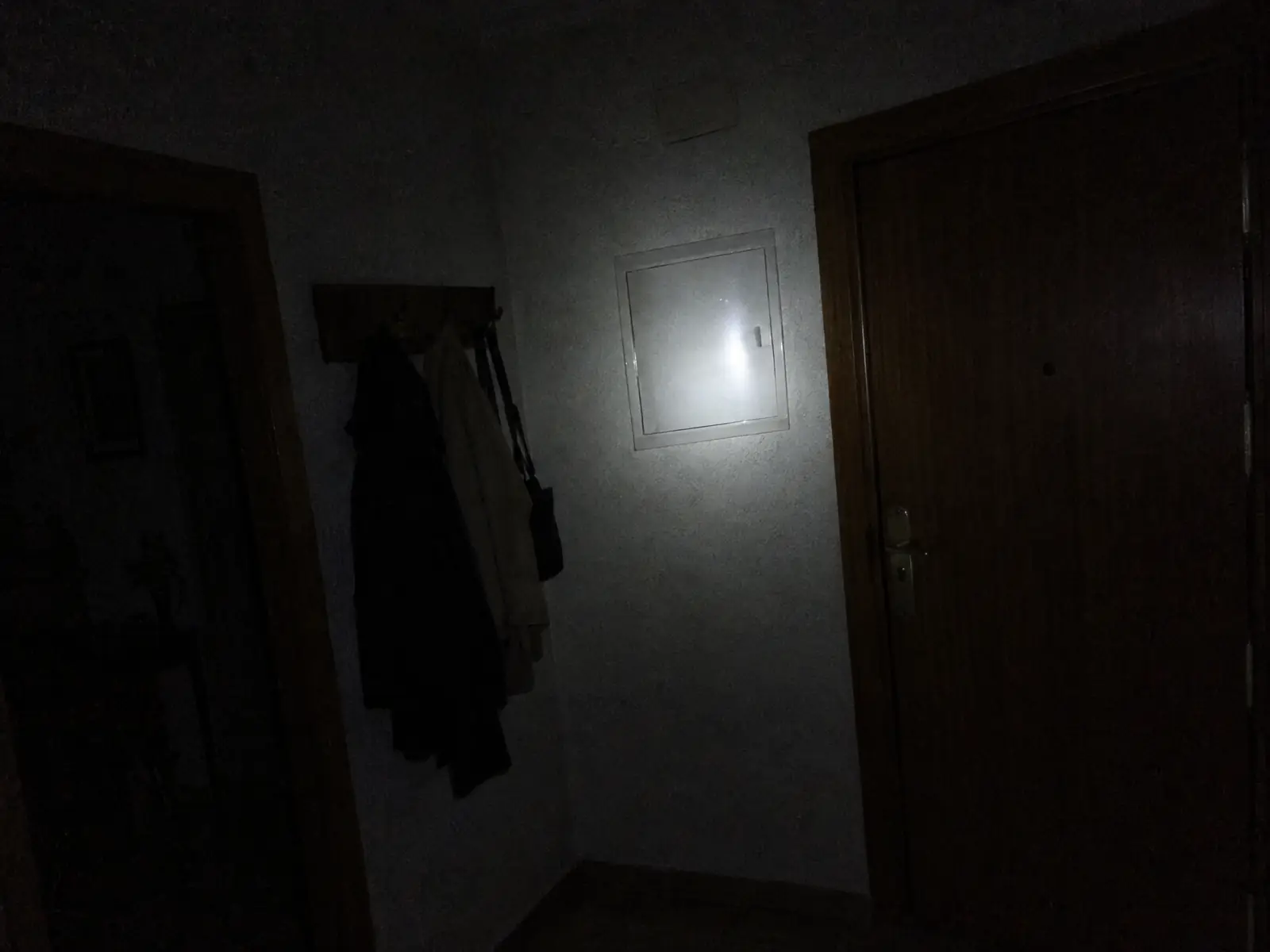 Recibidor de un piso a oscuras con la linterna de un móvil iluminando la tapa del cuadro eléctrico junto a la puerta