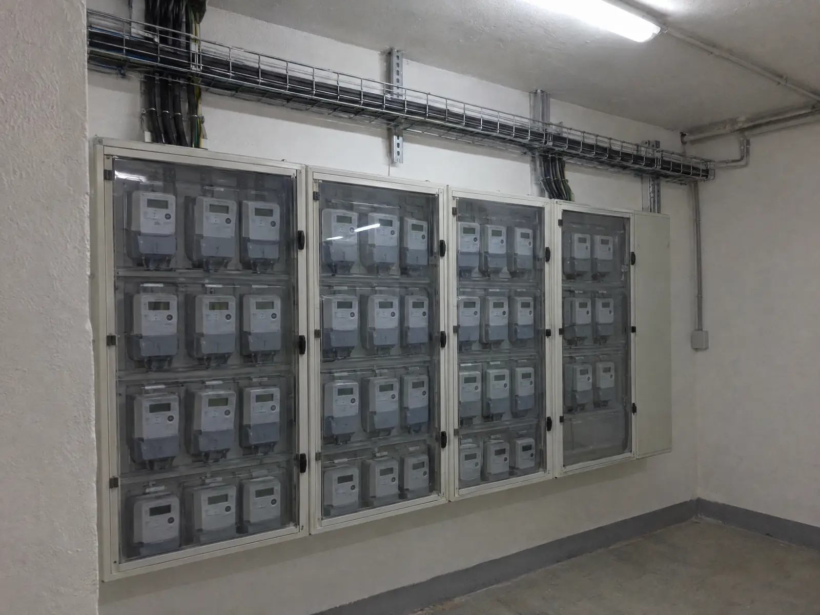 Cuarto de contadores de una comunidad con cuatro armarios de puertas transparentes llenos de contadores digitales y bandeja de cables