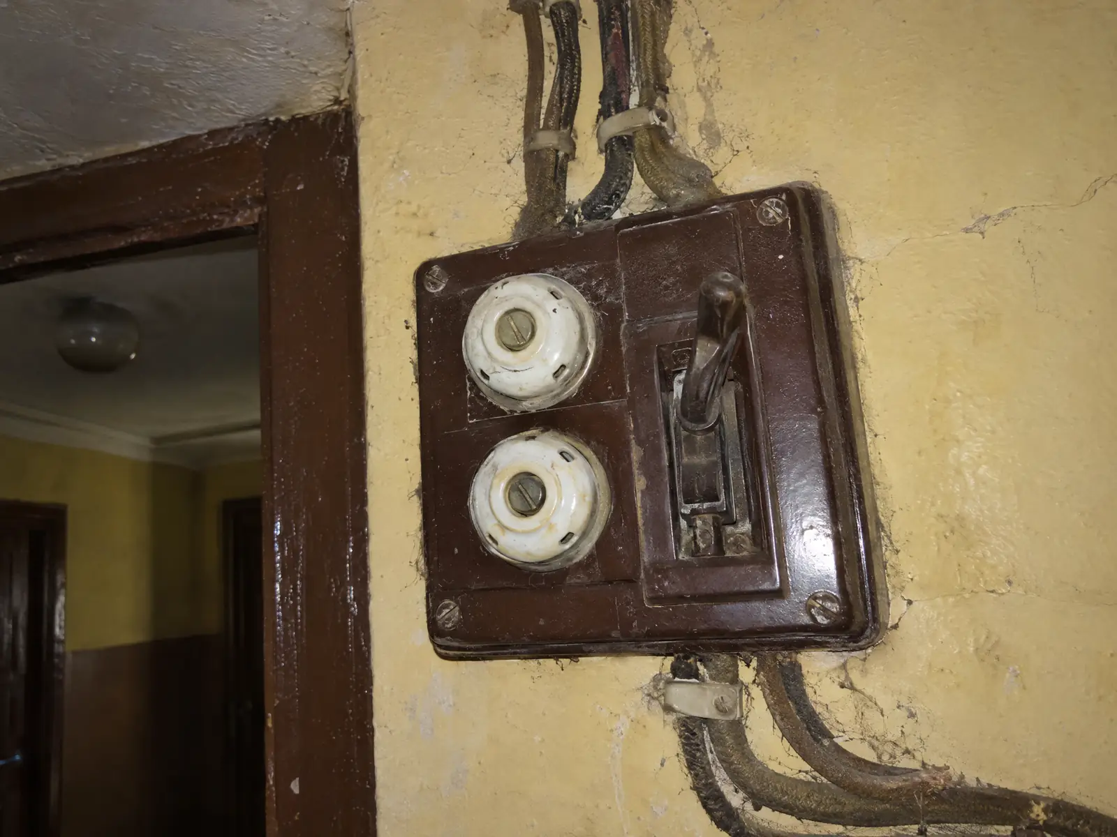 Cuadro antiguo de baquelita marrón con dos fusibles de porcelana, un interruptor de palanca y cables con funda de tela