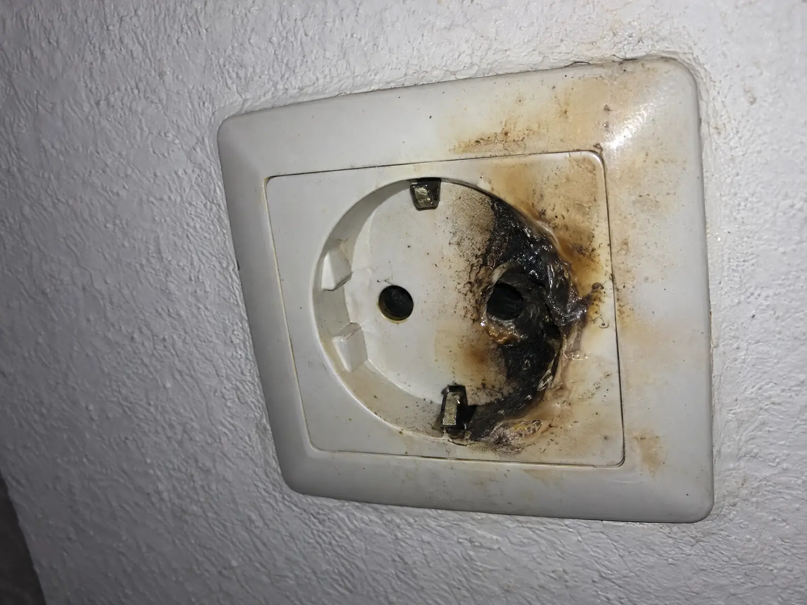 Enchufe de pared con un alveolo ennegrecido, el plástico derretido y marcas de quemado en la placa