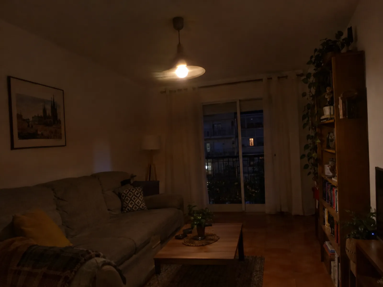 Salón en penumbra por la noche iluminado solo por una lámpara de techo con una bombilla que brilla de forma irregular